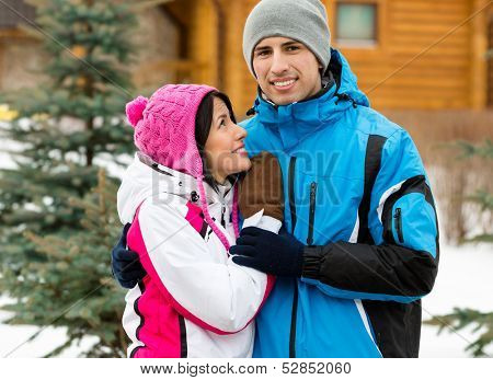 Half-length portrait of embracing couple who wears warm caps and jackets during winter vacations