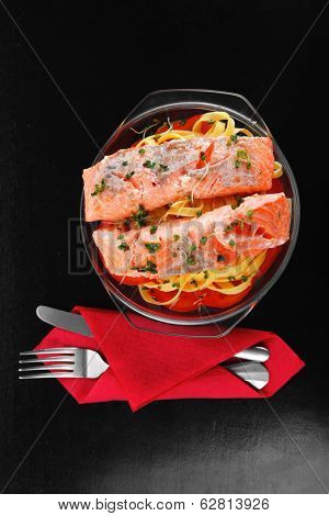 fresh fried natural pink salmon on italian traditional tagliatelle backed with tomato and vegetables served over black wooden table