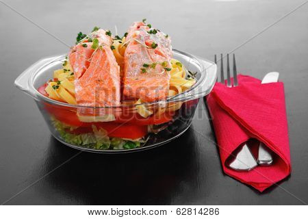 fresh fried natural pink salmon on italian traditional tagliatelle backed with tomato and vegetables served over black wooden table