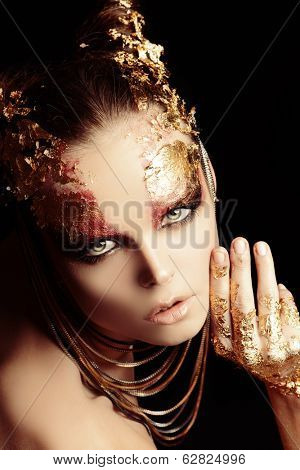 Art project: beautiful woman with golden make-up. Jewelry, make-up. Fashion. Over black background.