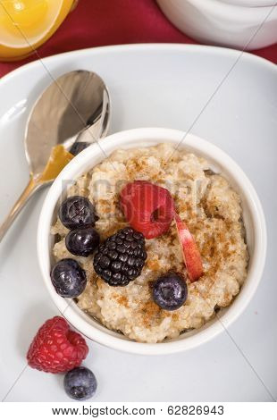 Delicious bowl of freshly made steal cut oatmeal served with fresh blackberries, blueberries, raspberries and apple with cinnamon and maple syrup