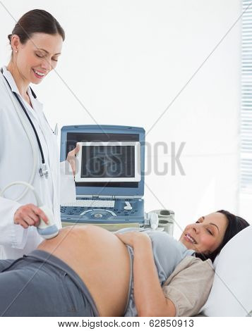 Smiling doctor performing ultrasound on stomach of expectant woman in hospital