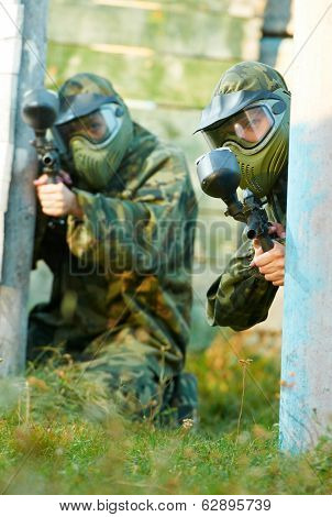 Two paintball sport players in prootective uniform and mask aiming and shoting with gun outdoors