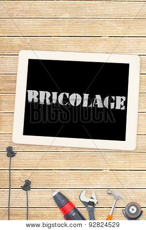 The word bricolage against tools and tablet on wooden background
