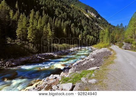 Pastoral in the Alpine mountain valley in Austria. Rapid mountain stream near the road. Cascades of cold water at the source of the famous Krimml waterfalls.