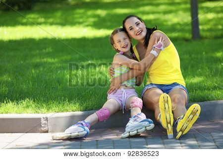 Young mom with her 6 years old child rollerskating in park