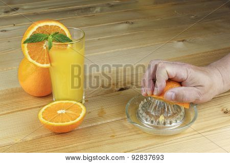 A hand squeezing juice from an orange on a manual glass squeezer. Set on a wooden planked table.