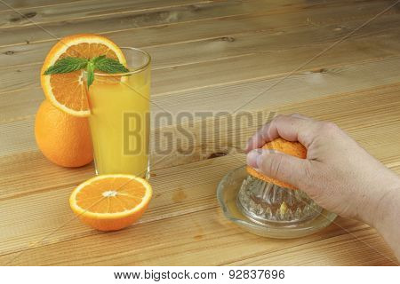 A hand squeezing juice from an orange on a manual glass squeezer. Set on a wooden planked table.