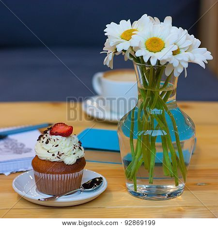Cupcake On The Plate And Chamomile In A Vase On The Table