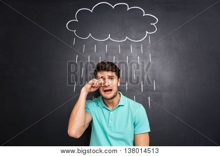 Unhappy disappointed young man crying under the rain drawn on blackboard background