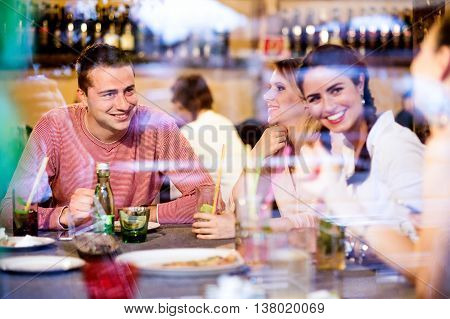 Young beautiful people with cocktails in bar or club, driniing and eating, having fun