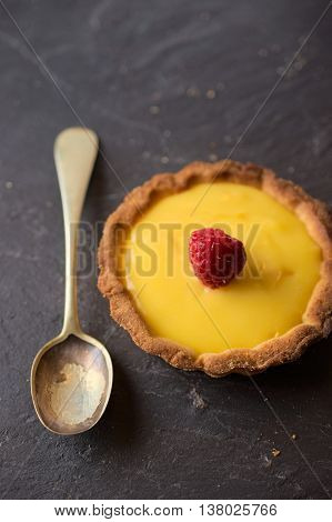 Delicious sweet dessert vanilla cream tart decorated with raspberry on dark stone slate. Selective focus on lemon slice. Concept of Home baking. Concept of home made desserts.