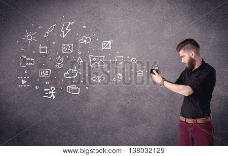 An elegant hipster guy trying to use a vintage camera with camera settings icons drawn on wall, like flash, white balace or ISO value concept