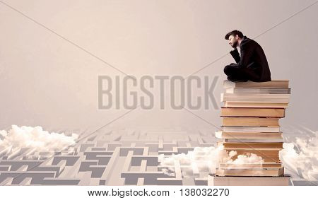 A serious businessman in suit sitting on a pile of giant books in front of a grey wall with clouds, labirynth