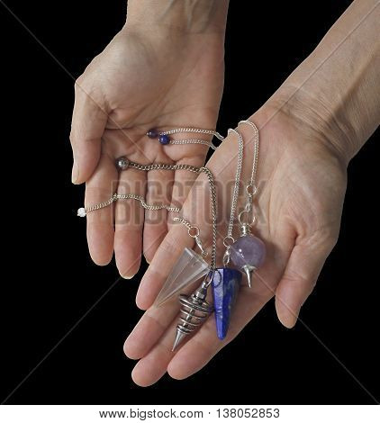 Which dowsing pendulum resonates with you - Female dowser holding four radionics pendants in an offering gesture on a plain black  background with copy space