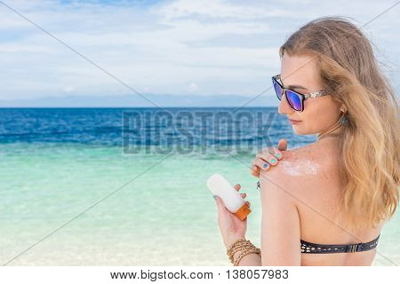 young woman applyng sun protector cream on her hand on the beach close to tropical turquoise sea under blue sky at sunny day