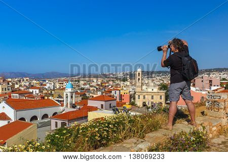 Photographer takes picture of medieval city with Orthodox cathedral Trimartiry from Schiavo Bastion in the sunny morning, Crete, Greece