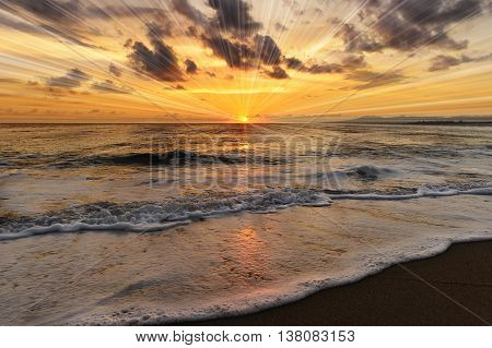 Ocean sunset sun rays is a brightly lit golden orange seascape with a burst of sun beams as a gentle wave rolling to the shore.
