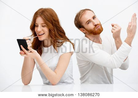 Funny redhead boy copying redhead girl putting on lip gloss over white background