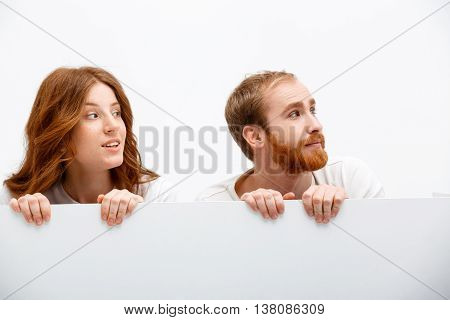 Funny redhead boy and girl hiding at white table smiling