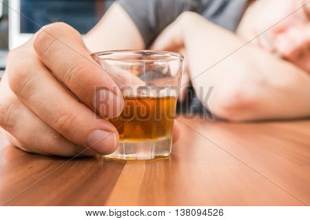 Alcoholic man is sleeping on table. Glass with alcohol in hand.