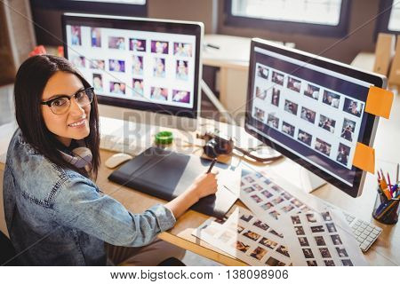 Female graphic designer using graphic tablet while working on computer at office