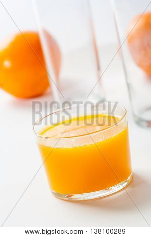 A delicious fresh glass of orange juice with ripe oranges on a white table.