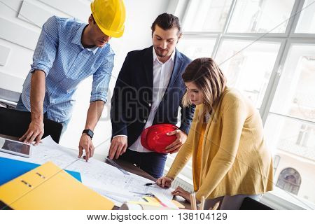 Tilt image of business people looking at blueprint on table at creative office