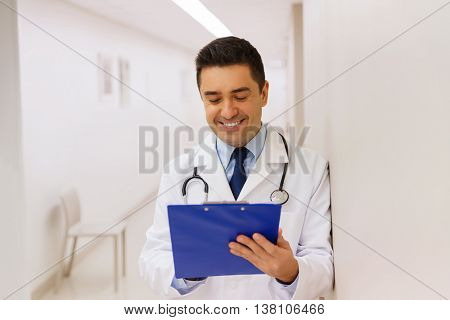 medicine, healthcare and people concept - happy smiling doctor writing to clipboard at hospital