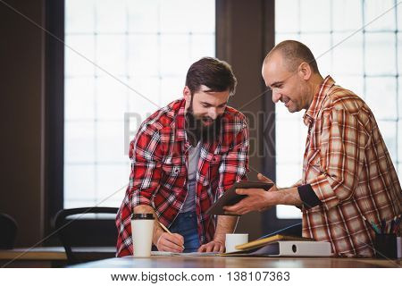 Smiling male coworkers discussing over digital tablet at table in creative office