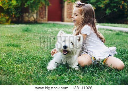 Child playing with English Highland White Terrier dog on grass in the backyard