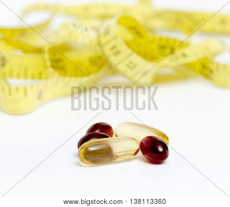 Picture of a Cod liver oil omega 3 gel and krill oil capsules in front of yellow tape measure