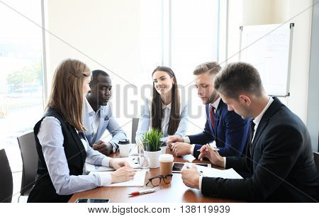 Young handsome woman gesturing and discussing something while his coworkers listening to him sitting at the office table
