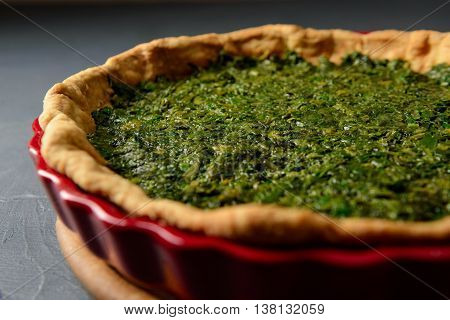 Close-up photo of baked tart dough with spinach in red ceramic tart pan, over gray textural surface, selective focus