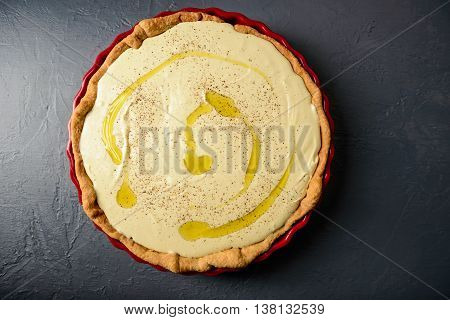 Close-up photo of tart with cream and olive oil, prepared for baking, over textural gray surface