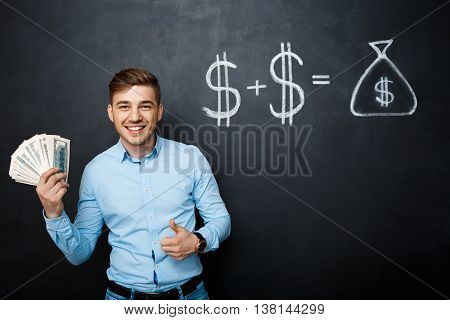 handsome man standing over blackboard. Holding dollars in his hands and smiling