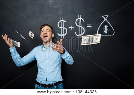 handsome man standing over blackboard. Holding and throwing dollars in his hands and smiling.