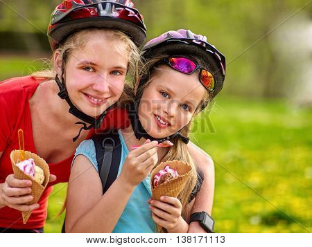 Bikes bicyclist girl. Girls wearing bicycle helmet with rucksack rides bicycle in summer park. Happy girls biking eating ice cream cone . Bicyclist is looking at camera.