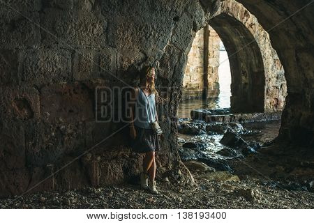 Young blond tourist woman stading in ancient stone shipyard and looking at the sea in the Old city, Alanya, Meditarranean region, Turkey.
