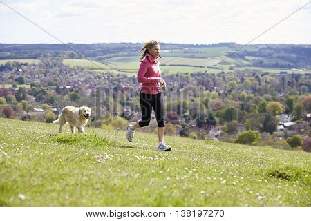 Mature Woman With Golden Retriever Jogging In Countryside