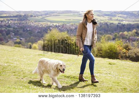 Mature Woman Taking Golden Retriever For Walk In Countryside