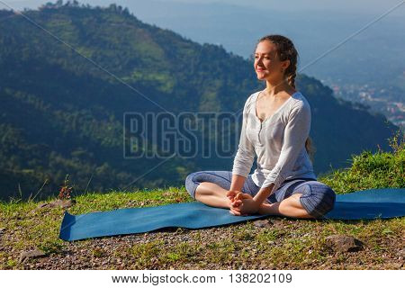 Sporty fit woman practices yoga asana Baddha Konasana - bound angle pose outdoors in HImalayas mountains in the morning with sky. Himachal Pradesh, India