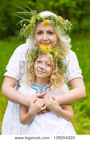 Beautiful and happy mum and daughter with wreaths on the head outdoors in the summer