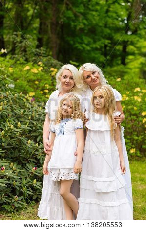 Beautiful cute blonde girls standing near flowers. Happy family outdoors in summer