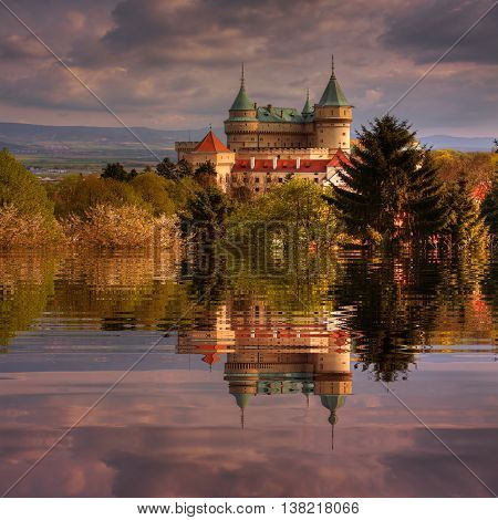 Romantic castle during the sunfall near the lake with water reflection