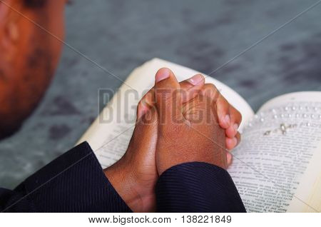 Man folding hands praying with open bible lying in front, seen from behind models head, religion concept.