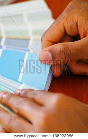 Closeup hands holding palette, colormap spread out in front of white computer keyboard, designer concept.