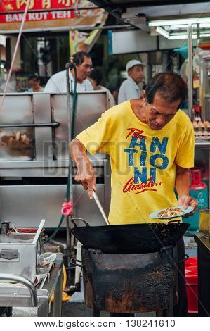GEORGE TOWN MALAYSIA - MARCH 22: Senior man cooks kway teow noodles in asian wok at the Kimberly Street Food Night Market on March 22 2016 in George Town Penang Malaysia.