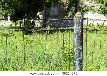 A fence made of rusty metal rods. Very old and rusty. A long time outdoors. The background is blurred (green grass).