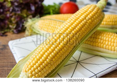 Ripe yellow corn cob with green leaves on brown wooden board